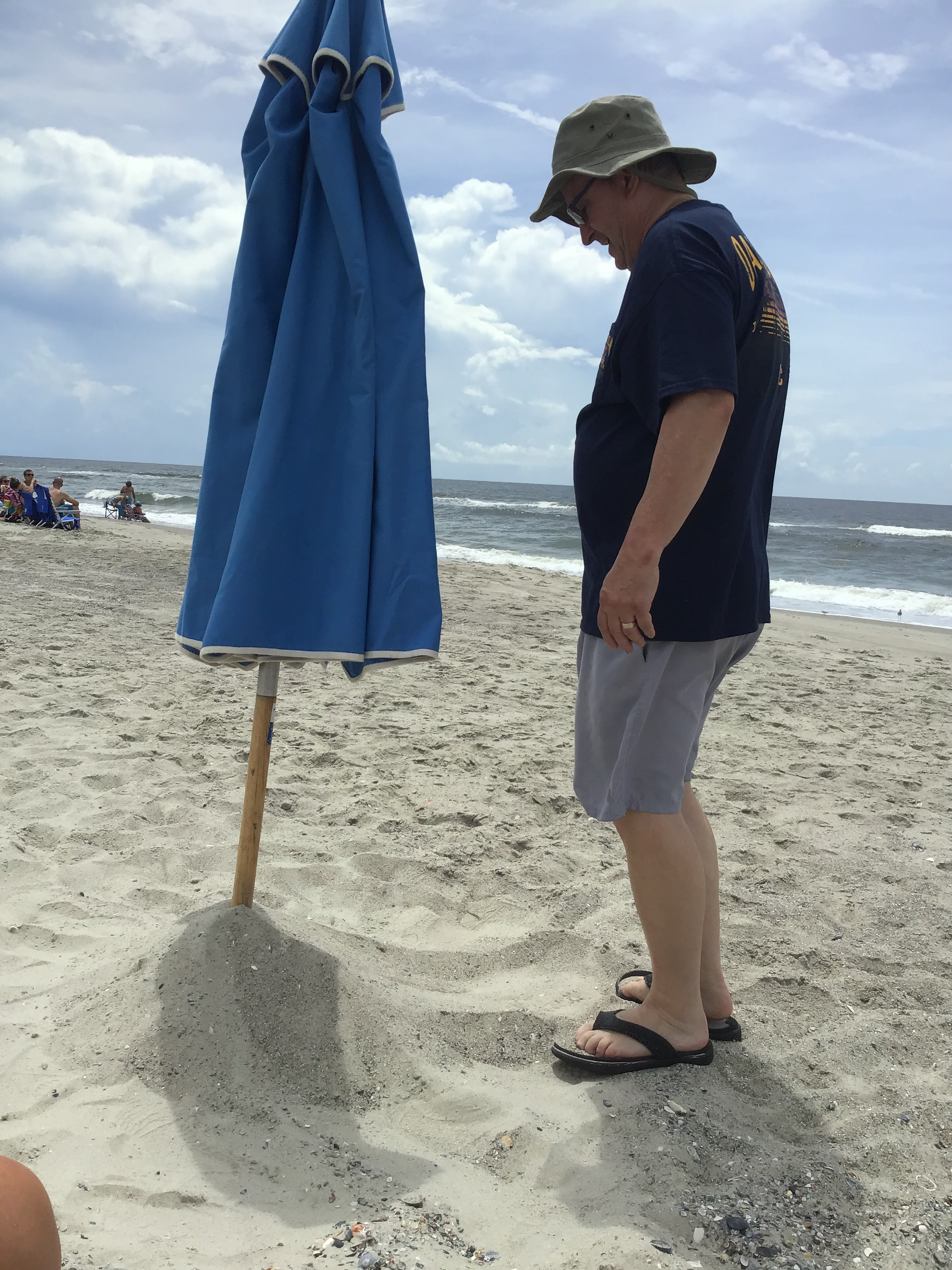 Gene Curtis is an old hand at putting up the umbrella!                             Location:  Sandpiper Cottage, Oak Island, NC                                 Source: Julane Crabtree                                Date: 28 Jul 2023