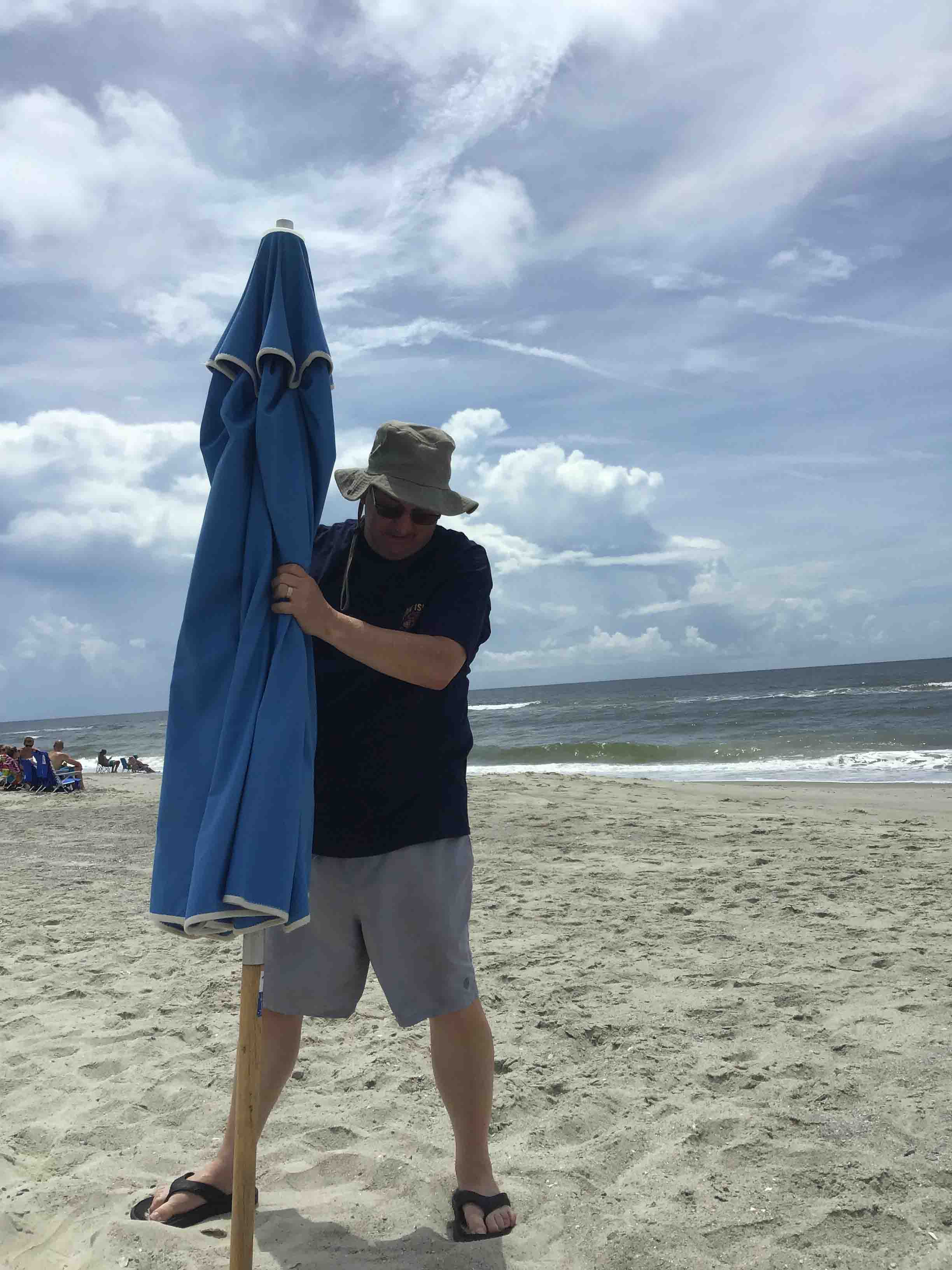 Gene Curtis is an old hand at putting up the umbrella!                             Location:  Sandpiper Cottage, Oak Island, NC                                 Source: Julane Crabtree                                Date: 28 Jul 2023