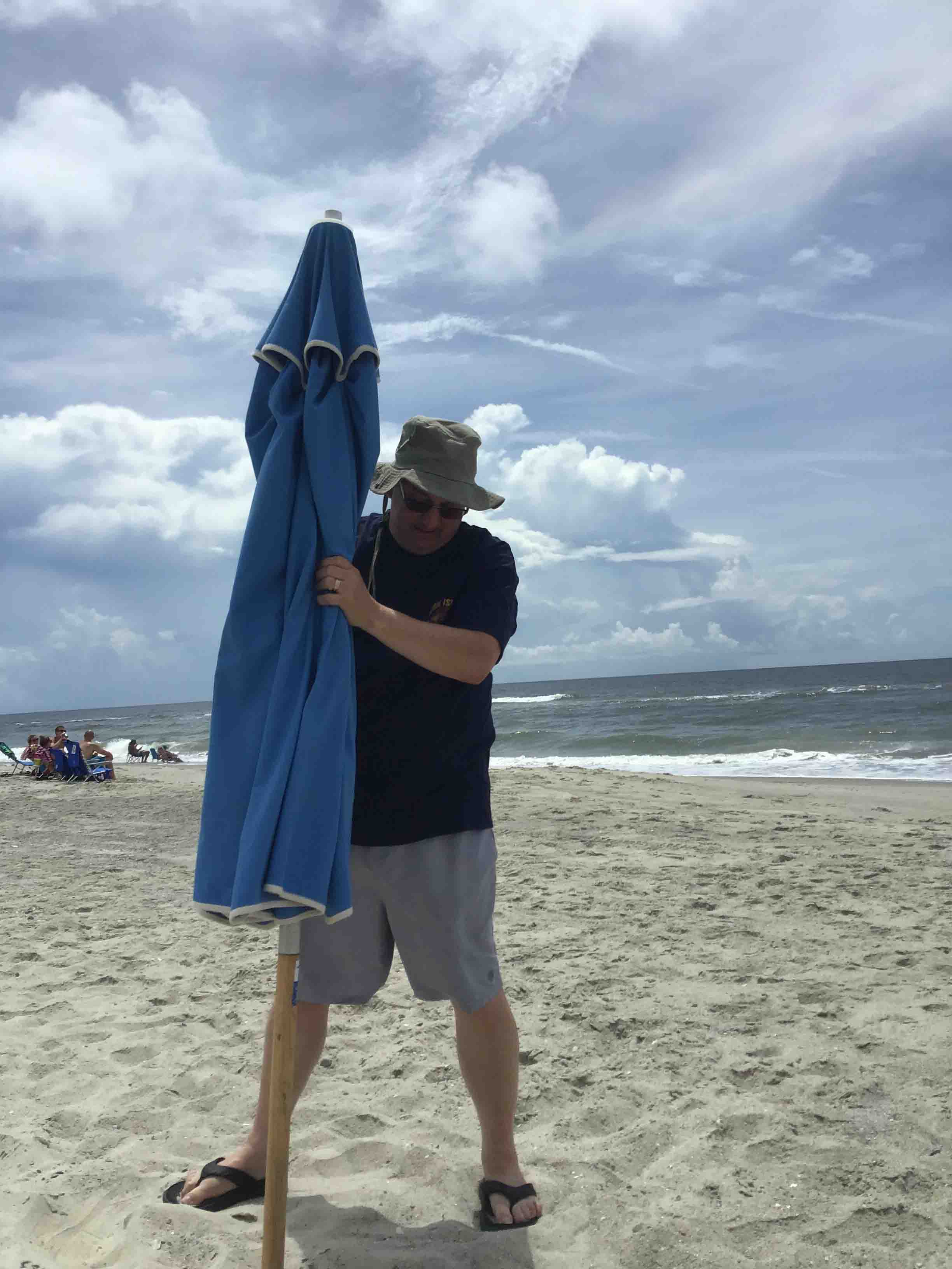 Gene Curtis is an old hand at putting up the umbrella!                             Location:  Sandpiper Cottage, Oak Island, NC                                 Source: Julane Crabtree                                Date: 28 Jul 2023